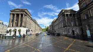 View east along Waterloo Place from the junction with Princes Street in Edinburgh, showing the section of road where essential sewer repairs will take place. Historic buildings line both sides of the street and the road surface looks wet.