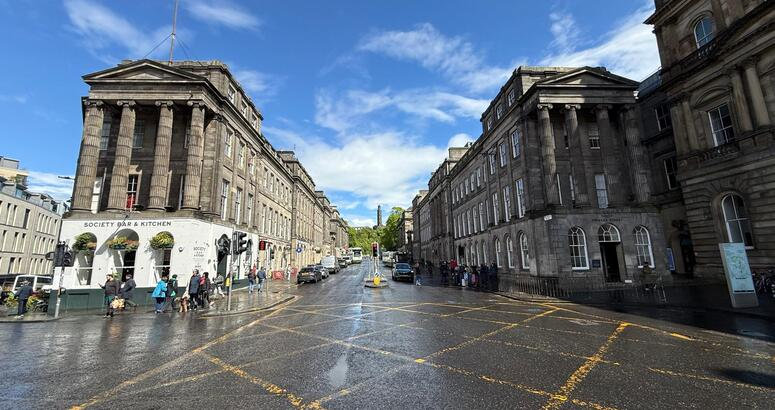 View east along Waterloo Place from the junction with Princes Street in Edinburgh, showing the section of road where essential sewer repairs will take place. Historic buildings line both sides of the street and the road surface looks wet.
