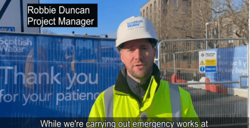 Construction worker with hard hat stands in front of construction site