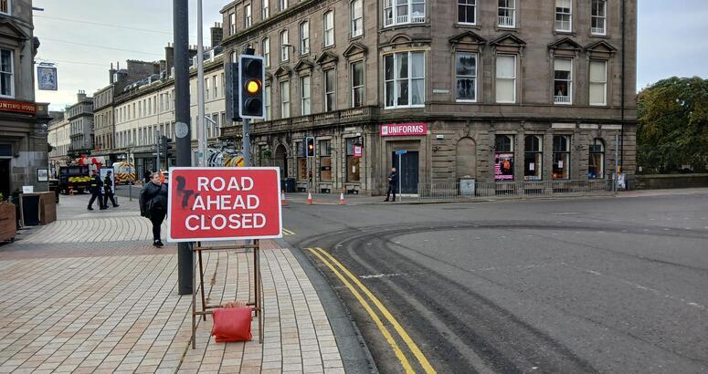 A 'Road ahead closed' sign sitting under traffic lights at the side of a road
