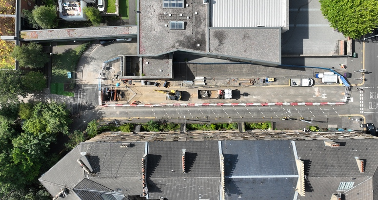 A bird's eye view of a road with construction work. Buildings line the street on either side.