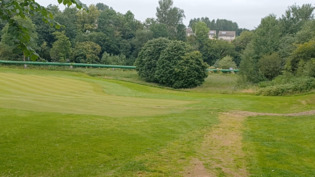 Grassy golf course with green pipe and building in background