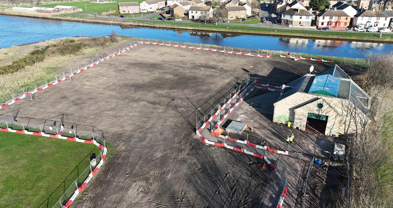 The newly paved walkway at the perimeter of the site of works at Esk Waste Water Pumping Station in Musselburgh is shown. The works are adjacent to a playing field.