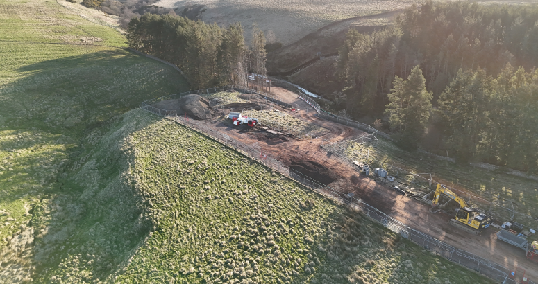 Aerial view of a construction site surrounded by wooded areas with machinery and vehicles at work
