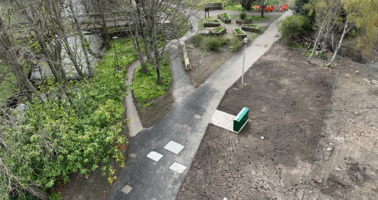 Drone footage of pathway with soil on right hand side and greenery and trees on left