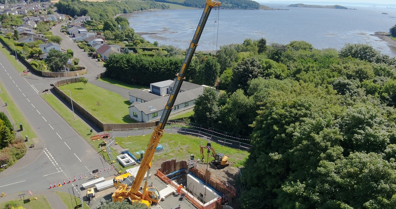 A large crane lifts equipment into place on a residential road near the coastline