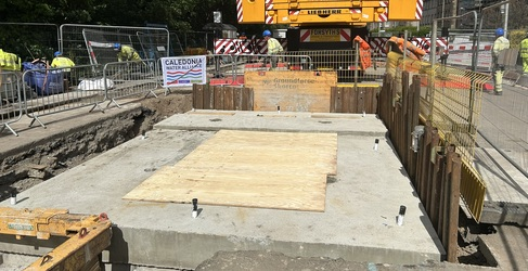 A concrete lid is shown on top of a large excavation within a construction site. A crane is visible in the background