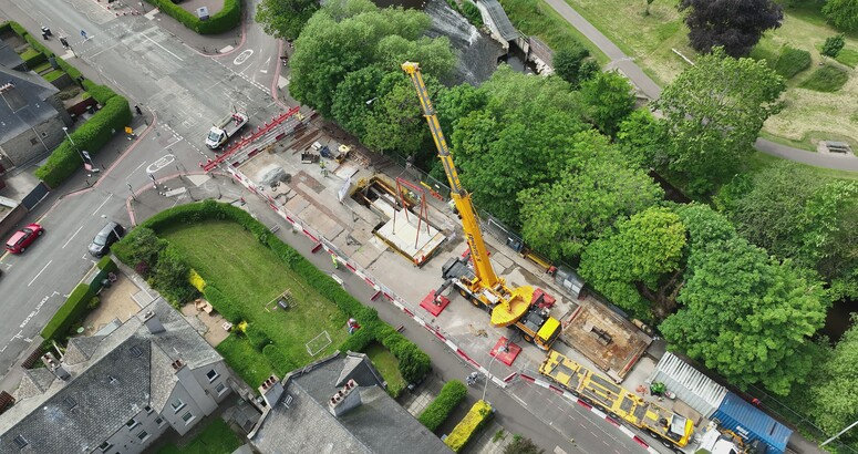 A large crane is shown lowering the lid on the site of major construction works on a residential street