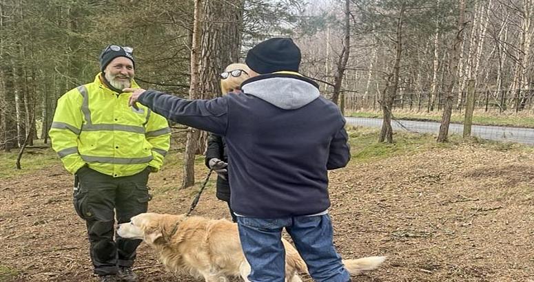 SW team member standing chatting to 2x visitors in the woods surround Gladhouse Reservoir. One visitor has back to camera and is pointing out something, while the other customer looks down at their dog