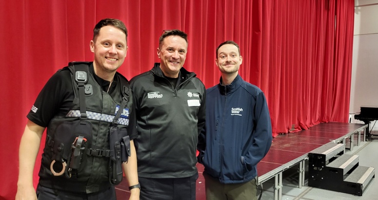 Reservoir Ranger Josh pictured on right with 2 males on left of him. Centred is a male from Scottish Fire and Rescue Service, then on left is a male from Police Scotland. All are in their uniforms with a red curtain back drop which was the school stage,