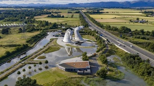 Image shows aerial view of a burst water main with water surrounding The Helix and the Kelpies in Falkirk and a motorway running alongside with countryside and mountain backdrop