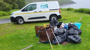 Scottish Water van parked in front of reservoir with pile of rubbish bags and various litter items on grass in front.