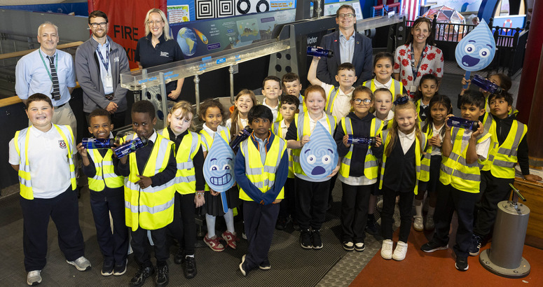 Group photo of Dunard Primary Children, teacher Mr Montgomery, Glasgow Science Centre reps Gillian Land and Joe Oxley - Gleister, Alex plant and Lorna Neilson standing beside water exhibit at Glasgow Science Centre.