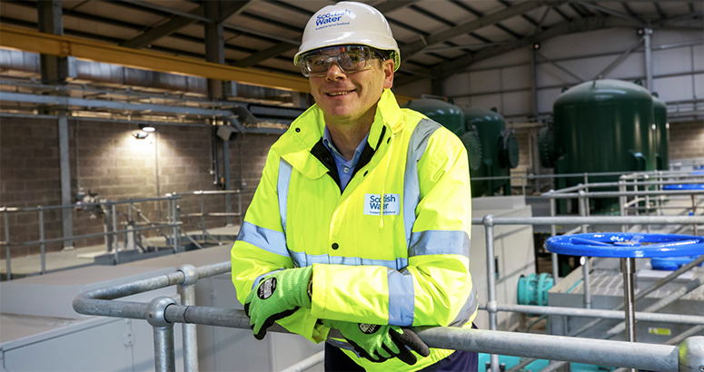 Scottish Water CEO Alex Plant in hi viz and hat leaning on railings inside a new pumping station at Ibrox