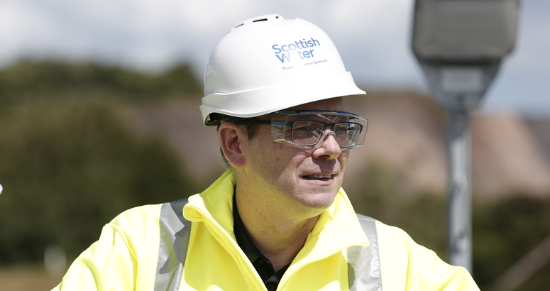Scottish Water CEO Alex Plant in hard hat and hi vis PPE outside.