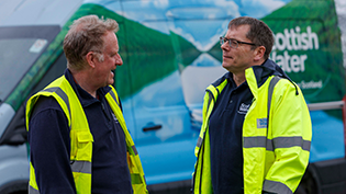 Scottish Water CEO Alex Plant chats to colleague Richard Bowman with both in hi viz jackets in front of a Scottish Water van