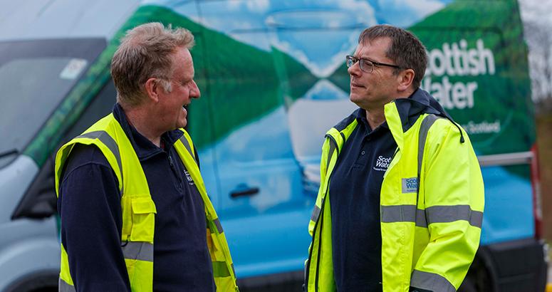 Scottish Water CEO Alex Plant chats to colleague Richard Bowman with both wearing hi viz jackets in front of a  Scottish Water van