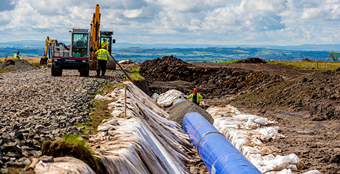 Large blue pipe in the ground with a digger beside it